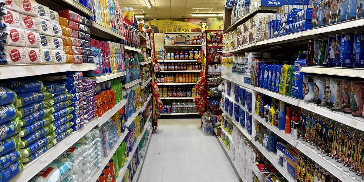 El pasillo del hogar: detergente y jabón de un lado y la pared de veladoras del otro, con velas de santos y de colores