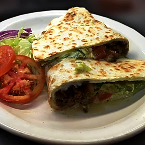 Una quesadilla dorada partida en dos, con carne, queso y guacamole